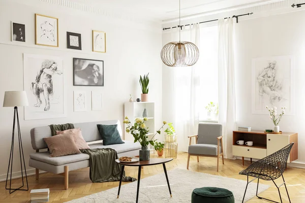 Tapis chaud sur parquet de salon tendance intérieur avec fauteuils élégants, table basse en bois, canapé gris et galerie d'affiches sur mur blanc — Photo