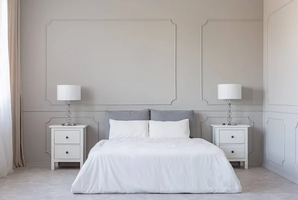White bedding on king size bed, copy space on empty grey wall