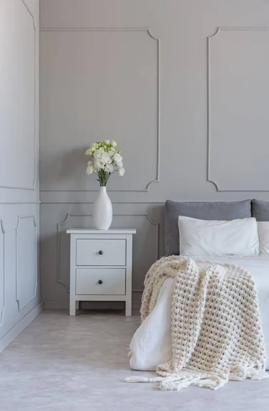 Růže v bílé stylové váze na dřevěné noční stolku se spodky vedle útulné postele s přikrývkou — Stock fotografie