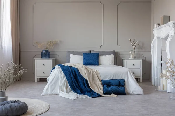 Белый камин, две тумбочки с выдвижными ящиками и двуспальная кровать с бензиновым сине-белым постельным бельем — стоковое фото