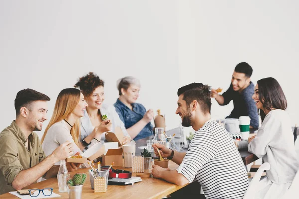 Jóvenes compañeros felices en la corporación hablando y almorzando juntos — Foto de Stock