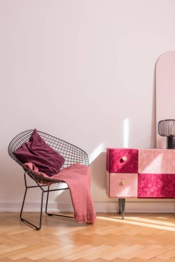 Bordo yastık ve pembe battaniye şık süet kapalı kabine yanında trendy metal koltuk, boş beyaz duvara kopya alanı ile gerçek fotoğraf