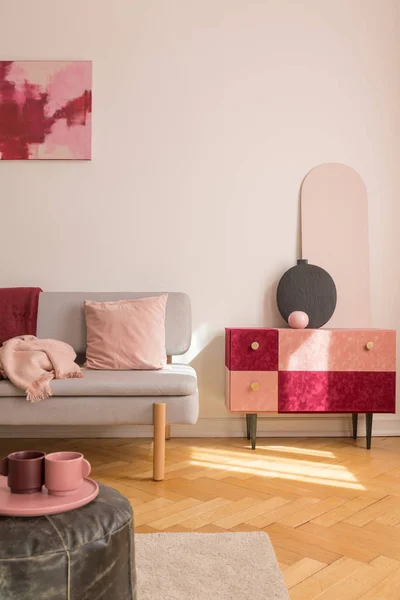 Вертикальный вид красивого замшевого шкафа с черной модной вазой рядом с модным серым диваном с розовой подушкой и бургундским одеялом — стоковое фото