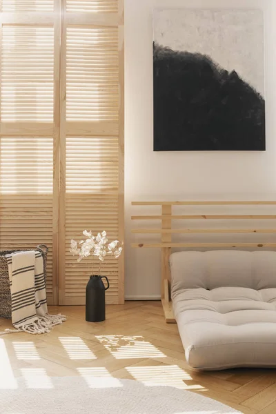 Černá a bílá malba nad béžovou skandinávskou postelí z futonu v přirozeném interiéru ložnice, skutečná fotka se skvrnou na prázdné stěně — Stock fotografie
