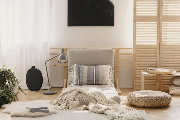 White warm blanket and pattern pillow on beige futon in stylish natural bedroom interior, real photo with mockup on the empty wall — стоковое фото