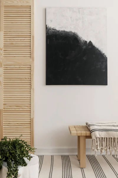 Pintura moderna en blanco y negro en la pared de la elegante sala de espera con banco de madera con manta a rayas y planta verde en la esquina — Foto de Stock