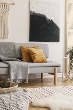 Sarı yastıklar ve sıcak battaniye ile gri şık kanepe ile moda oturma odası iç duvarında beyaz el yapımı makrome ve modern boyama dikey görünümü