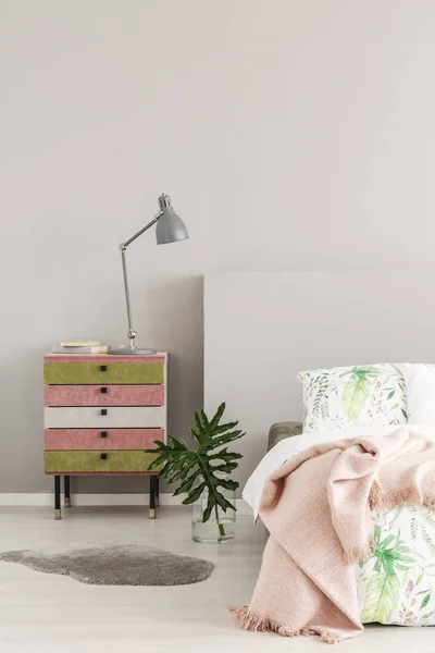 Olijfgroen en pastel roze gekleurde nightstand naast glazen vaas met blad in eenvoudige slaapkamer interieur, kopieerruimte op de lege grijze muur — Stockfoto