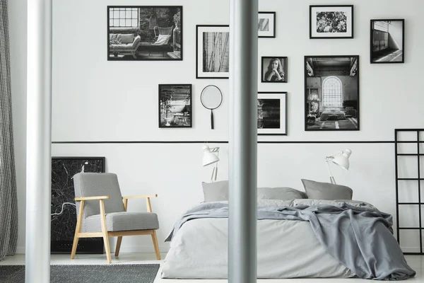 木制扶手椅旁边的床在白色的卧室内部与画廊的照片在墙上。真实照片 — 图库照片