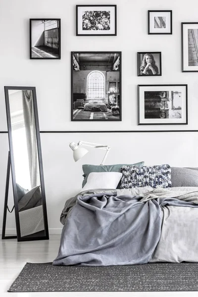 Specchio accanto al letto con lenzuola grigie in bianco camera da letto minimale interno con manifesti. Foto reale — Foto Stock