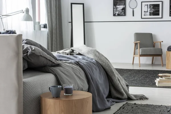 Tasses sur table en bois à côté du lit gris dans l'intérieur de la chambre avec miroir et fauteuil. Une vraie photo — Photo