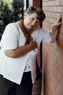 Kırmızı tuğla duvar yanında yardım bekleyen kalp krizi ile zayıf Büyükanne