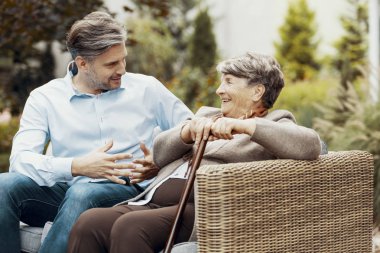 Yürüyüş sopa ile gülümseyen kıdemli kadın terasta konuşan adam dinlerken