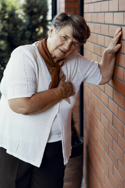 Слабка бабуся з серцевим нападом чекає на допомогу біля стіни з червоної цегли — стокове фото