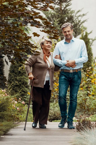 Smiling man walking with happy elderly woman in the garden — Stock Photo, Image