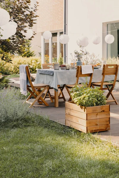 Real photo of a garden with a table, chairs, lamps and wooden box with plants — Stock Photo, Image