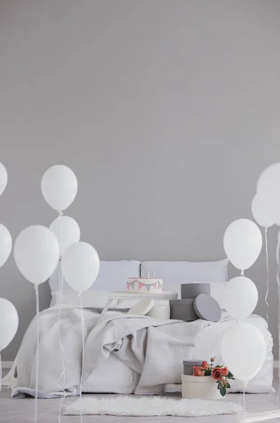 Elegant sovrum med King size-säng med grå sängkläder, födelsedags tårta och vita ballonger, riktiga foto med kopierings utrymme på tom vägg — Stockfoto