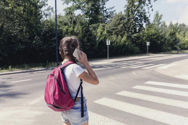 Gadis dengan ransel menggunakan smartphone saat berjalan melalui penyeberangan pejalan kaki — Stok Foto