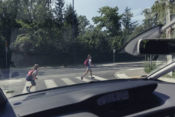 从一辆汽车上看到的孩子们的背包跑过人行横道到学校 — 图库照片