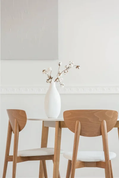 Close-up van bloemen in witte vaas op houten eettafel met stoelen — Stockfoto