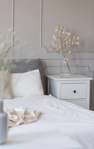 Mesita de noche con flores en jarrón de cristal junto a la cama con sábanas blancas — Foto de Stock