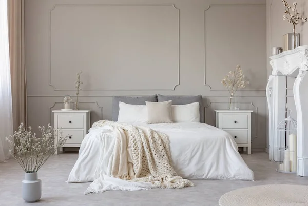 Кровать королевского размера с белыми простынями и одеялом между двумя деревянными тумбочками цветов в вазах — стоковое фото