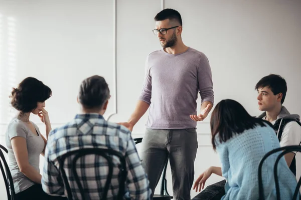 Ung ledsen man pratar med gruppen människor under psykoterapi — Stockfoto