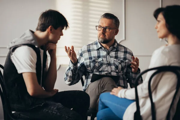 Psychologist talking to depressed teenager and his mum during therapy session — Stock Photo, Image