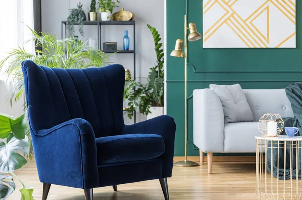 Blauwe fauteuil naast grijze Scandinavische sofa in tropisch geïnspireerde interieur met groene en gouden kleuren — Stockfoto