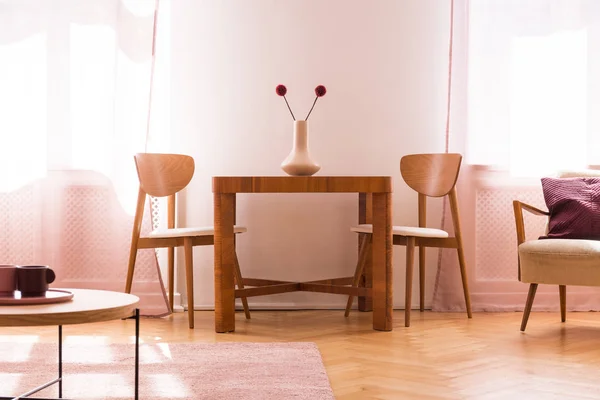 Sillas de madera en la mesa con flores en el interior luminoso salón con sillón. Foto real —  Fotos de Stock