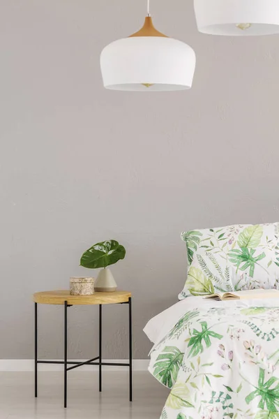 Lampada bianca sopra foglia in piccolo vaso su comodino in legno in camera da letto scandinava, copiare spazio sulla parete grigia vuota — Foto Stock