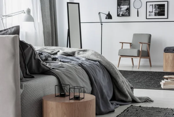 Bougies sur table en bois à côté du lit gris dans l'intérieur de la chambre avec fauteuil et lampe. Une vraie photo — Photo