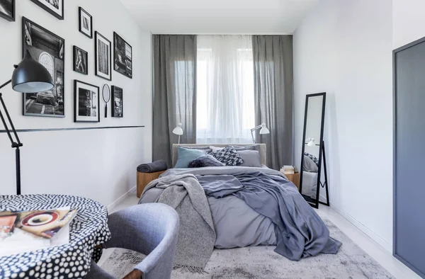 Mirror next to bed with grey sheets in bedroom interior with black lamp and posters. Real photo — Stock Photo, Image