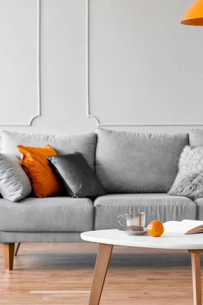 Graues Sofa mit Kissen und Couchtisch mit Orange im Wohnzimmer. echtes Foto — Stockfoto