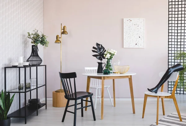 Estante de metal con platos y vasos en el moderno comedor interior con mesa redonda con flores en jarrón y hoja negra en jarra — Foto de Stock