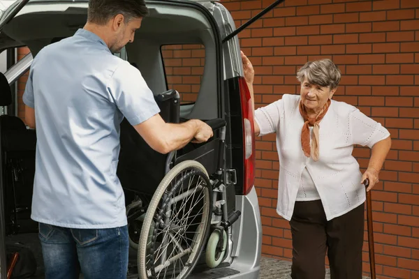 Aide soignant tenant un fauteuil roulant dans la voiture pour femme âgée handicapée avec bâton de marche — Photo