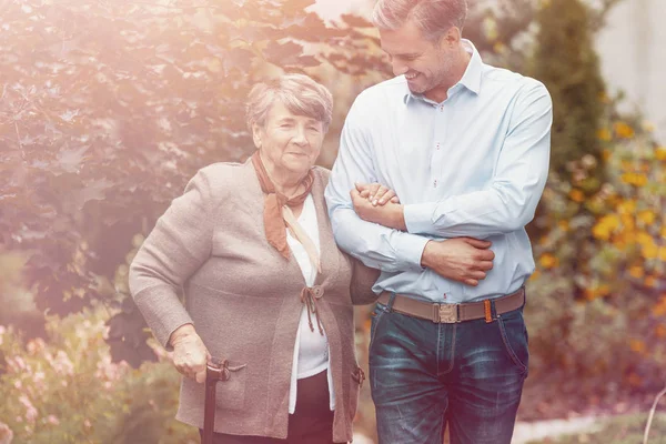 Smiling son relaxing on outdoor with happy mother with walking stick — Stock Photo, Image