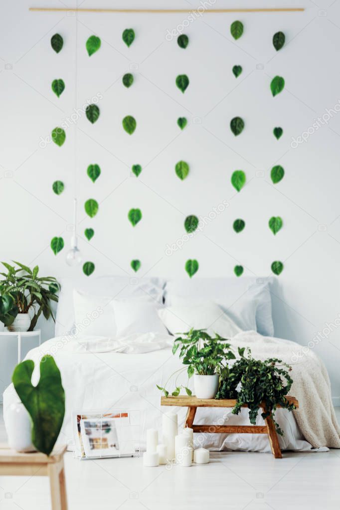 Green leafs on white wall of cozy bedroom interior