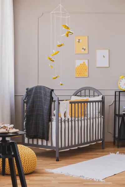 在灰色木制婴儿床上方安装黄色和黑色蜜蜂，带毯子和枕头 — 图库照片