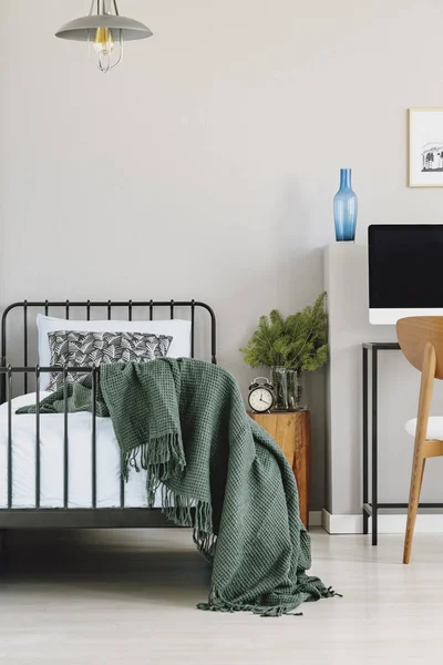 Copy space on empty grey wall of chic bedroom interior with industrial single bed with blue sheets, pattern pillow and dark green blanket — стоковое фото