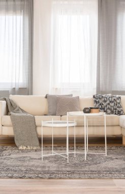 Gri yastık ve battaniye ile rahat kanepe önünde iki beyaz endüstriyel sehpa