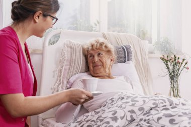 Onun sitesinde pembe üniformalı yararlı hemşire hastane yatağında yatan pozitif üst düzey hasta