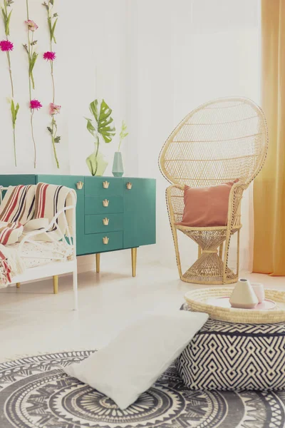 Круглый этно ковер на белом полу стильного интерьера спальни с зеленой мебелью и плетеным креслом павлина — стоковое фото