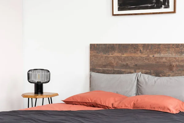 Bed with wooden headboard, coral sheets and black industrial lam — Stock Photo, Image