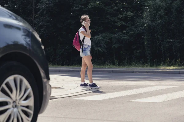 Adolescente na travessia de pedestres na frente de um carro falando pelo telefone — Fotografia de Stock