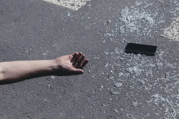Humans hand on street next to broken glass and mobile phone