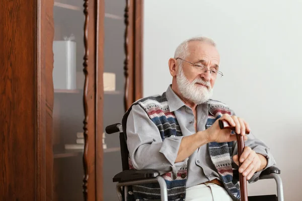 Пожилой человек, сидящий на инвалидном кресле и поддерживающий себя тростью — стоковое фото