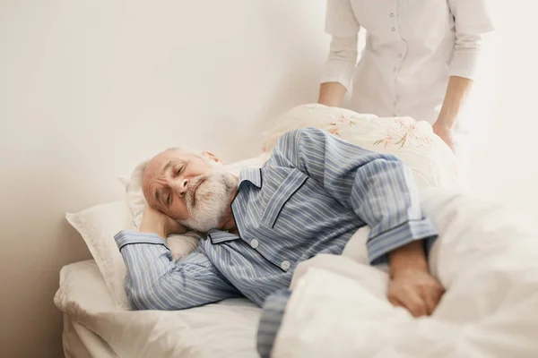 Больной старик в синей пижаме лежит в постели в доме престарелых — стоковое фото