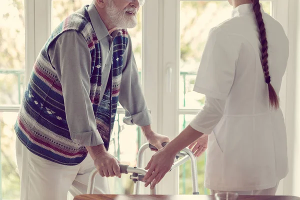 Paciente mayor en residencia de ancianos con enfermera servicial en uniforme blanco — Foto de Stock