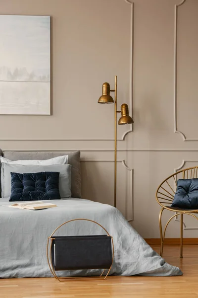 Стильная золотистая лямка рядом с кроватью размера king size с синим постельным бельем и темно-синими подушками — стоковое фото